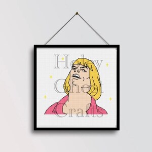 May include: Cross-stitch art of a cartoon character with blonde hair and a pink top, looking upwards with a strained expression. The text "Holy Crafts" is visible. The artwork is framed in a black frame and hung by a wire.