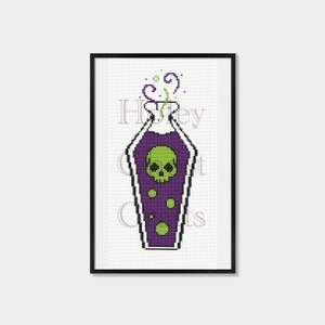 May include: A cross-stitch pattern of a purple potion bottle with a green skull inside and green smoke coming out of the top. The bottle is in a black frame.