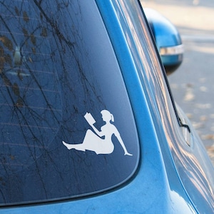 May include: A blue car with a white silhouette sticker of a person sitting and reading a book on the back window.
