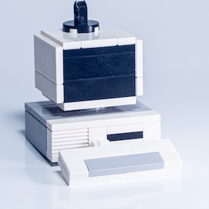 Peut inclure: Une décoration de Noël en forme d'ordinateur Lego blanc avec un écran noir et un crochet argenté.