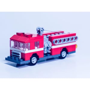 May include: A red and gray toy fire truck made of Lego bricks. The truck has a ladder, a hose, and a water tank.