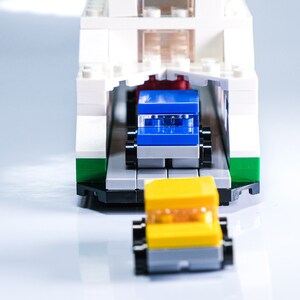 K&ouml;nnte beinhalten: Eine wei&szlig;e Spielzeugf&auml;hre mit einem blauen Auto und einem gelben Auto, die aus der Garage der F&auml;hre fahren.