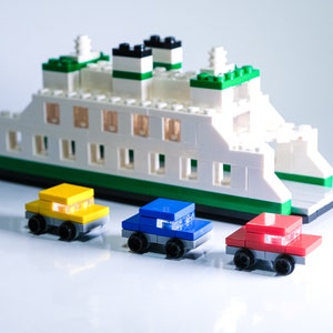 K&ouml;nnte beinhalten: Ein wei&szlig;es, gr&uuml;nes und blaues Spielzeug-F&auml;hrschiff mit drei Spielzeugautos davor. Die Autos sind gelb, blau und rot.