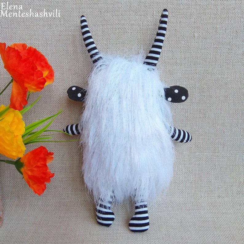 May include: A white furry toy with black and white striped legs and horns. The toy has black ears with white polka dots.