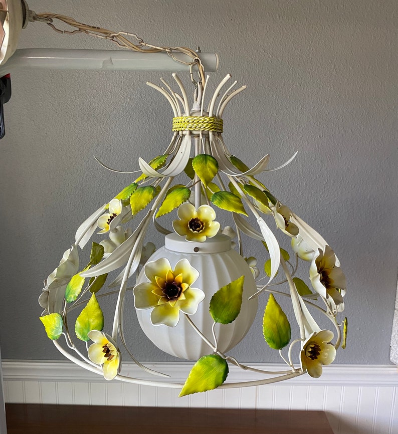 May include: White metal chandelier with yellow and green floral accents. The chandelier has a white globe-shaped light fixture.