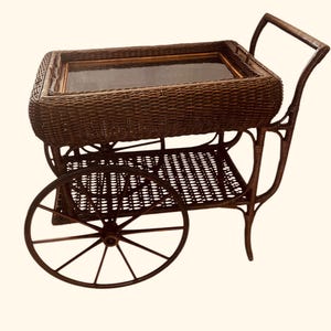 May include: A brown wicker serving cart with a glass top and two wheels. The cart has a lower shelf and a handle on the back.