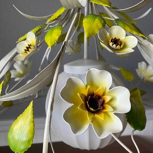 May include: White metal chandelier with yellow and green flowers. The chandelier has a white frosted glass shade.