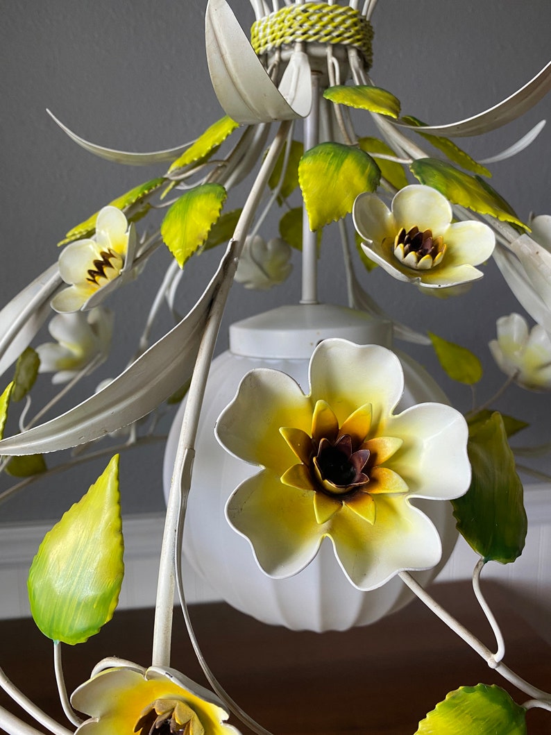 May include: White metal chandelier with yellow and green flowers. The chandelier has a white frosted glass shade.