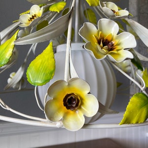 May include: White metal chandelier with yellow and green flowers. The chandelier has a white globe-shaped light fixture.