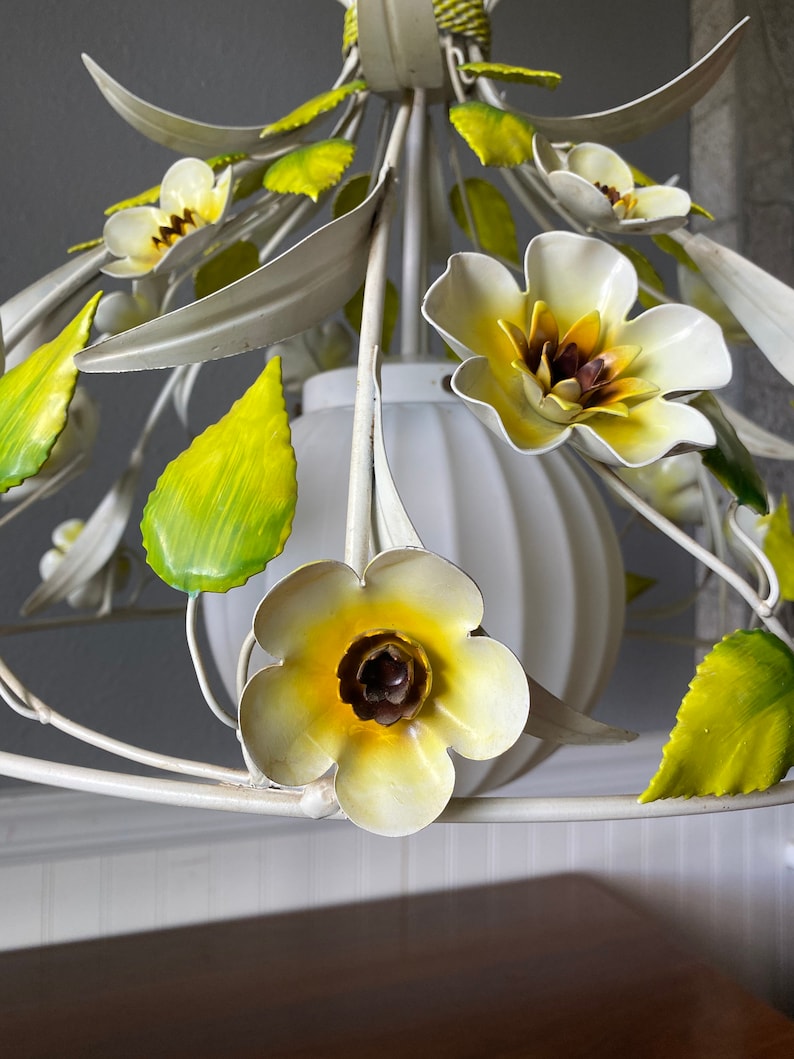 May include: White metal chandelier with yellow and green flowers. The chandelier has a white globe-shaped light fixture.
