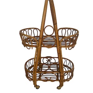 May include: A two-tiered rattan serving cart with a handle. The cart has a natural brown color and features a decorative woven design. It has four wheels for easy mobility.