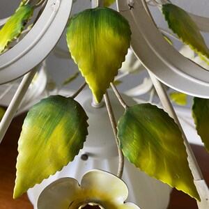 May include: White metal chandelier with green and yellow leaves and a white flower with a yellow center.