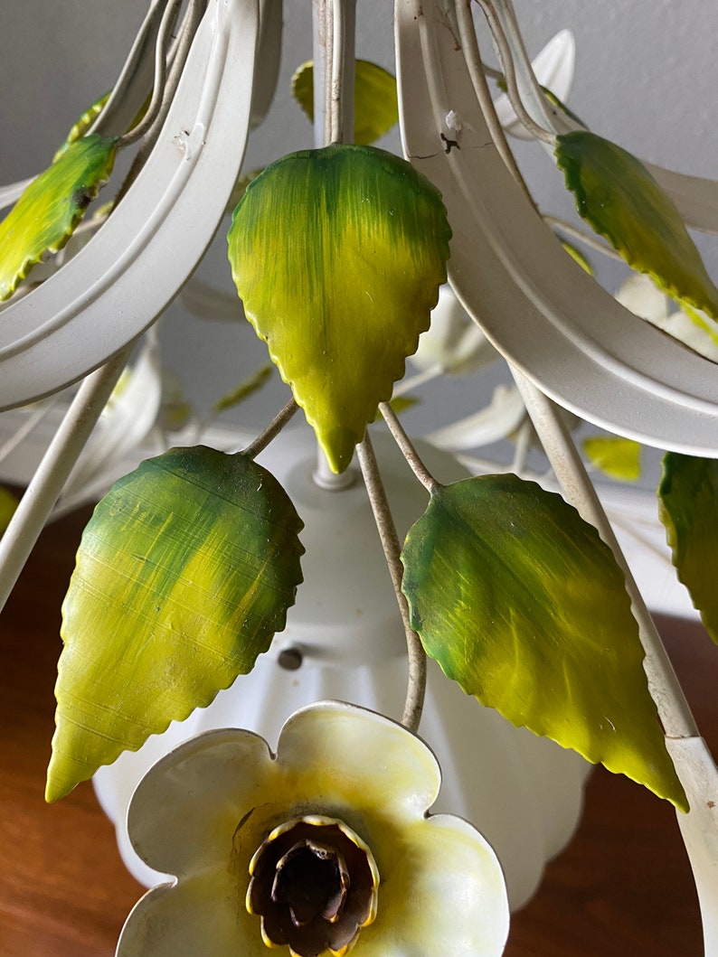 May include: White metal chandelier with green and yellow leaves and a white flower with a yellow center.