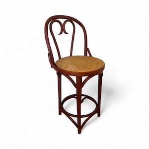 May include: A dark brown wooden bar stool with a woven rattan seat. The back of the stool features a decorative heart-shaped design. The stool has a circular footrest and is set against a white background.