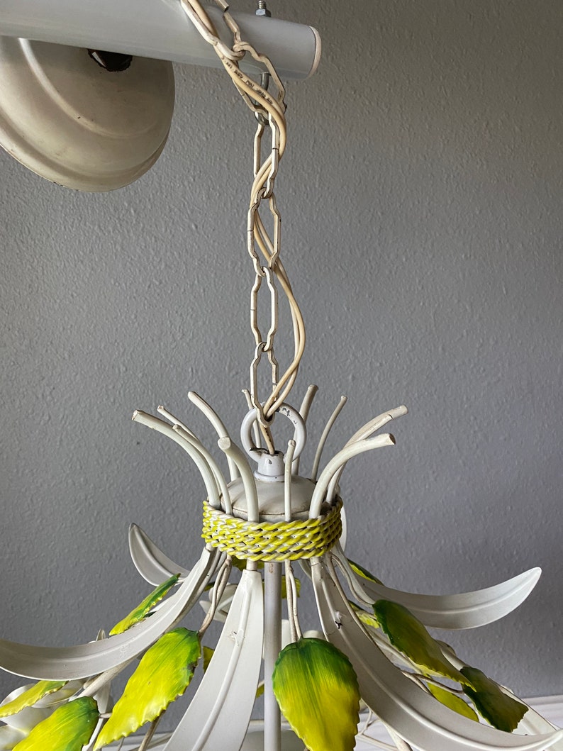 May include: White metal chandelier with green leaves and a woven band around the top. The chandelier is hanging from a chain.