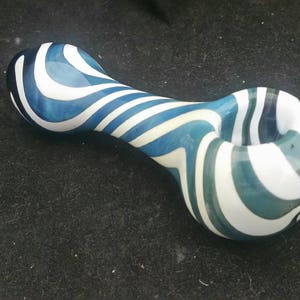 May include: A white and blue glass pipe with a swirling pattern. The pipe is shaped like a traditional pipe with a bowl and a stem.