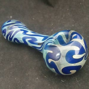 May include: A blue and white glass pipe with a swirling pattern. The pipe is made of glass and has a bowl on one end and a mouthpiece on the other.