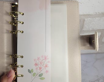 May include: A white page with the text "5K Savings" at the top. The page is decorated with a pink floral design and is bound into a beige leather planner.