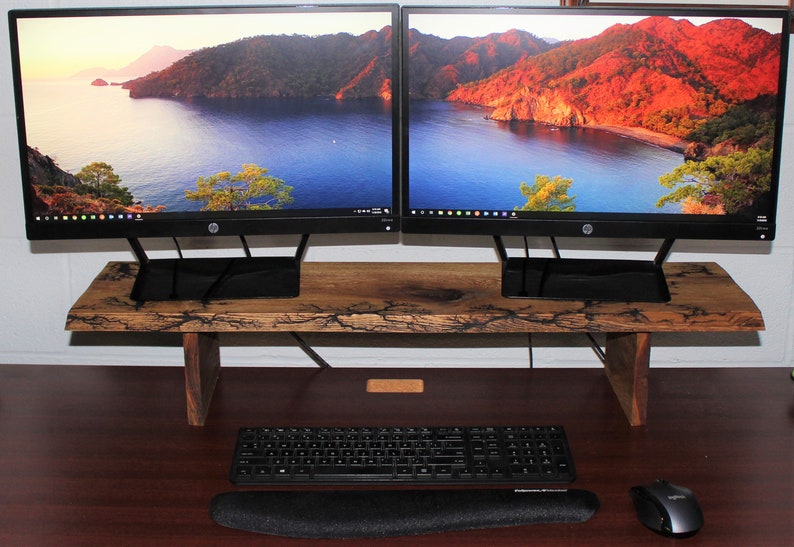 May include: A wooden monitor stand with a natural wood finish and black metal legs. Two black computer monitors are on top of the stand. A black keyboard and mouse are on a wooden desk below the stand.