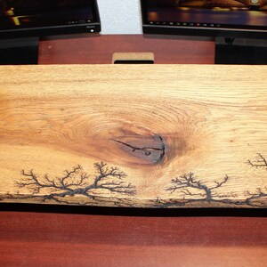 May include: A natural wood desk top with a live edge and a knot in the center. The wood has been treated with a dark brown stain and has a unique black lightning bolt pattern.