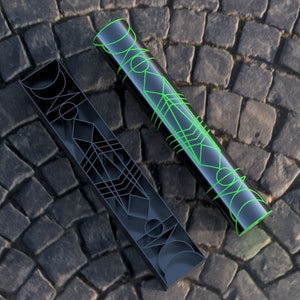 May include: Two black cylindrical containers with geometric patterns. The container on the left has a black and white pattern, while the container on the right has a green and black pattern.