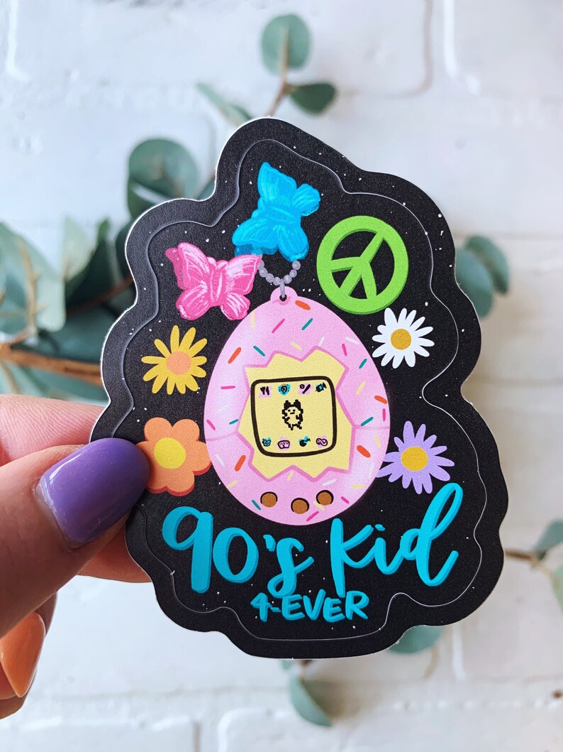 May include: A black and white sticker with a pink and yellow Tamagotchi, a peace sign, butterflies, and flowers. The text reads "90's kid 4ever".