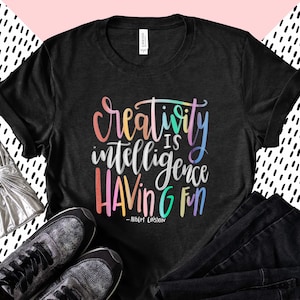 May include: Black t-shirt with a rainbow colored graphic that says "Creativity is intelligence having fun - Albert Einstein".