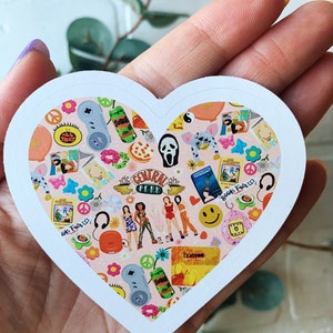 May include: A heart-shaped sticker with a pink background and a variety of 90s pop culture icons, including the Friends logo, a Scream mask, a Tamagotchi, and a Hanson CD. The sticker also features a variety of other 90s icons, such as peace signs, smiley faces, and flowers.