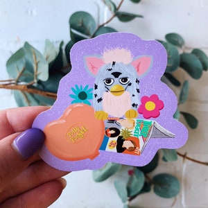 May include: A purple sticker with a fuzzy, gray and white toy, a pink heart with the words "Polly Pocket" on it, and a magazine with the words "Tiger Beat" on it.