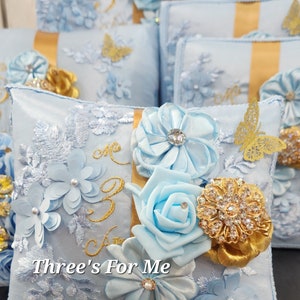 May include: Light blue satin pillow with gold embroidery and embellishments. The pillow features a large gold number "3" and the text "Three's For Me". The pillow is decorated with blue satin flowers, a gold butterfly, and gold rhinestones.