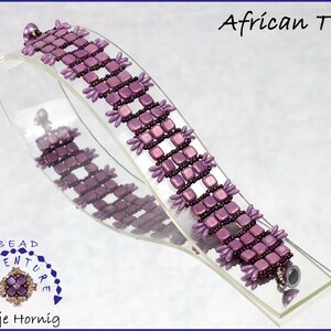 Könnte beinhalten: Ein violettes Perlenarmband mit quadratischem Fliesenmuster. Das Armband befindet sich auf einem durchsichtigen Präsentationsständer. Der Text "African Tiles Kit" befindet sich in der oberen rechten Ecke des Bildes.