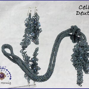 May include: A set of beaded jewelry featuring a long necklace and matching earrings. The necklace is made of small, dark blue beads and has a knotted design. The earrings are also made of dark blue beads and have a delicate, floral design. The jewelry is displayed on a white background.