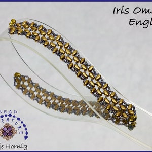 Pode incluir: Um bracelete de contas douradas e roxas com um padrão tecido. O bracelete é exibido em um suporte de acrílico transparente. O texto "Iris Omega English" é visível acima do bracelete.