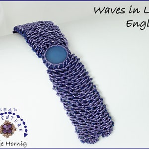 Könnte beinhalten: Ein lila-blaues Perlenarmband mit einem blauen Cabochon in der Mitte. Das Armband ist mit einem Wellenmuster gearbeitet. Das Armband ist mit "Waves in Lace English" beschriftet.