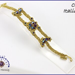 Könnte beinhalten: Goldfarbenes Perlenarmband mit violetten und blauen, schillernden Glasperlen. Das Armband befindet sich auf einem weißen Präsentationsständer. Der Text "Beadventure" und "Antje Hornig" ist unten links sichtbar. Der Text "Cecy Italiano" ist oben rechts sichtbar.