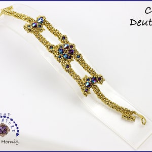 Könnte beinhalten: Ein goldenes Perlenarmband mit einem sich wiederholenden Muster aus kleinen goldenen Perlen und größeren, facettierten, regenbogenfarbenen lila und blauen Perlen. Das Armband wird auf einem klaren Acrylständer präsentiert. Der Text "Beadventure" und "Antje Hornig" ist in der linken unteren Ecke des Bildes sichtbar. Der Text "Cecy Deutsch" ist in der rechten oberen Ecke des Bildes sichtbar.