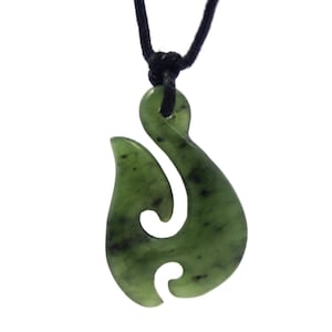 May include: A green jade pendant in a hook shape, suspended from a black cord. The pendant has a smooth, polished surface with dark green and black speckles. The cord is knotted at the top.