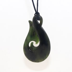May include: A green jade pendant in the shape of a traditional Maori fish hook, called a hei matau, on a black cord.