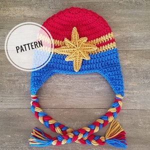 May include: A crocheted hat with a blue and red braided strap. The hat features a yellow star on a blue and red background. The hat is labeled "PATTERN".