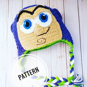 Puede incluir: Sombrero de crochet con una correa trenzada de color morado, verde y blanco. El sombrero presenta una cara de dibujos animados con ojos azules y una cara amarilla y verde. El texto "PATTERN" está escrito en un círculo blanco.