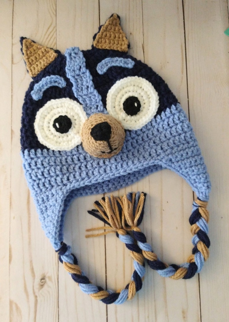 May include: Blue and brown crocheted hat with a cartoon dog face. The hat has a long braided cord.