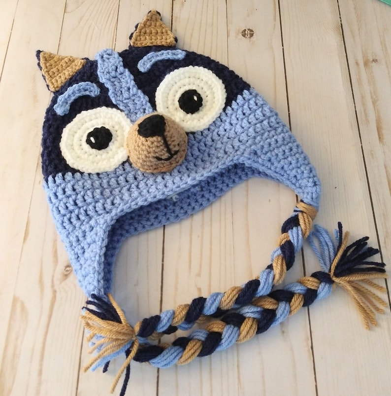 May include: Blue and brown crocheted hat with a cartoon animal face and braided ties.
