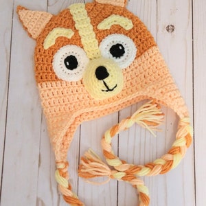 May include: A crocheted orange and yellow fox hat with a braided cord. The hat has a cute fox face with black eyes and a black nose.