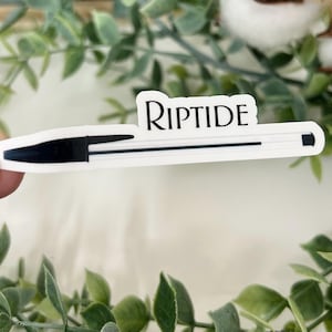 May include: A white sticker in the shape of a pen with the word "Riptide" in black script. The pen has a black tip and a black line down the center.