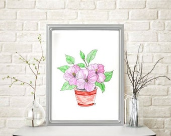 May include: A framed watercolor painting of pink flowers in a red pot with green leaves. The artwork is displayed in a silver frame and set against a white brick wall. The painting is on a white table.