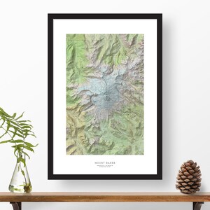 May include: A framed topographic map of Mount Baker, a mountain in Washington state. The map shows the mountain's elevation, trails, and surrounding landscape. The map is printed in shades of green, brown, and blue.