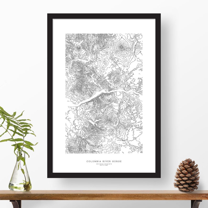 May include: Black and white topographic map print of the Columbia River Gorge, Oregon, USA. The print is framed in a black frame and is hanging on a white wall.