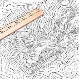 May include: A black and white topographic map print with concentric circles, resembling a mountain range. A wooden ruler is placed diagonally across the print. The print measures 24 x 36 inches.