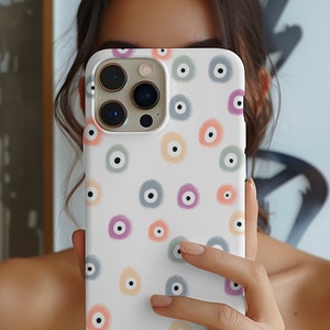May include: A white iPhone case with a colorful eye pattern. The case has a camera lens cutout and a white background with a repeating pattern of colorful eyes.