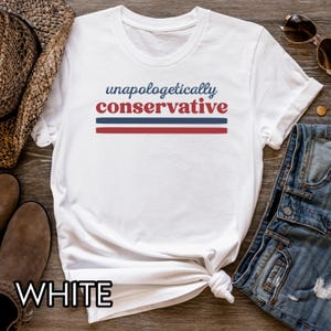 May include: White t-shirt with the text "unapologetically conservative" in blue and red. The text is above two horizontal stripes, one blue and one red. The word "WHITE" is printed at the bottom of the shirt.
